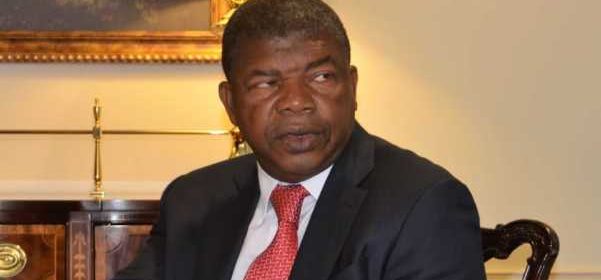 João Lourenço sentado em ambiente institucional, usando fato escuro e gravata vermelha, durante encontro político relacionado ao debate constitucional em Angola.